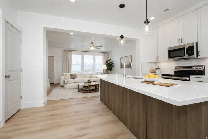 Spacious kitchen featuring a large island with a quartz countertop and wood-finish paneling, stainless steel appliances, a tile backsplash, and overhead pendant lighting