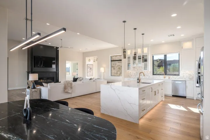 Kitchen with white cabinets, glass fronted cabinets, light stone countertops, an island with sink, and light wood-style flooring
