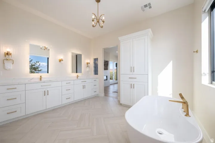 Full bathroom with double vanity, a freestanding bath, a chandelier, and parquet flooring
