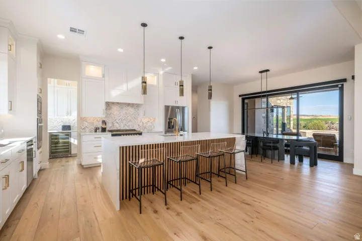 Kitchen with an island with sink, light wood-type flooring, backsplash, a kitchen breakfast bar, and wine cooler
