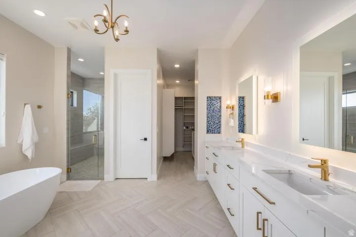 Bathroom featuring double vanity, a shower stall, a freestanding bath, a spacious closet, and hanging lights