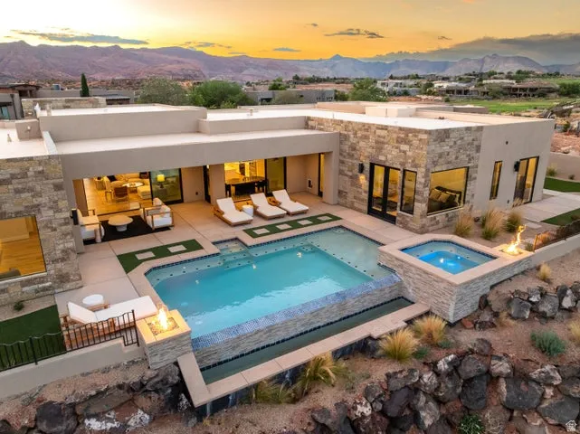 Back of house at dusk with an in-ground hot tub, an outdoor pool, a patio, and a mountain view