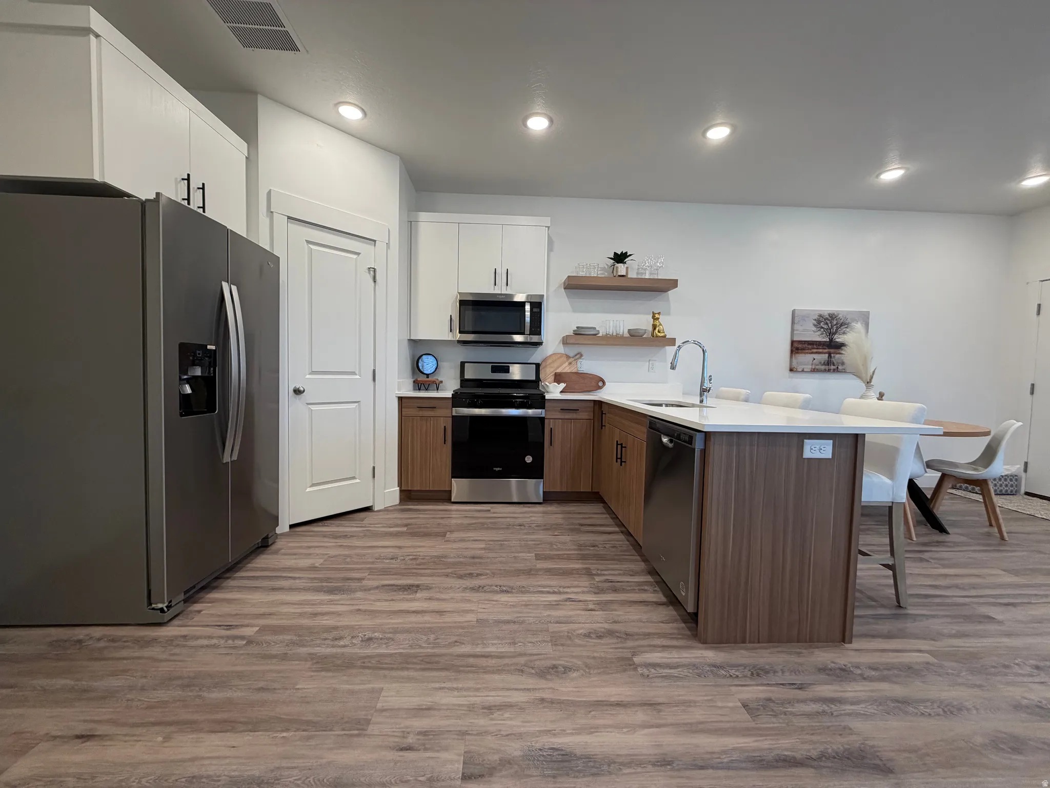 Kitchen with stainless steel appliances, a peninsula, open shelves, a breakfast bar area, and light wood-style floors
