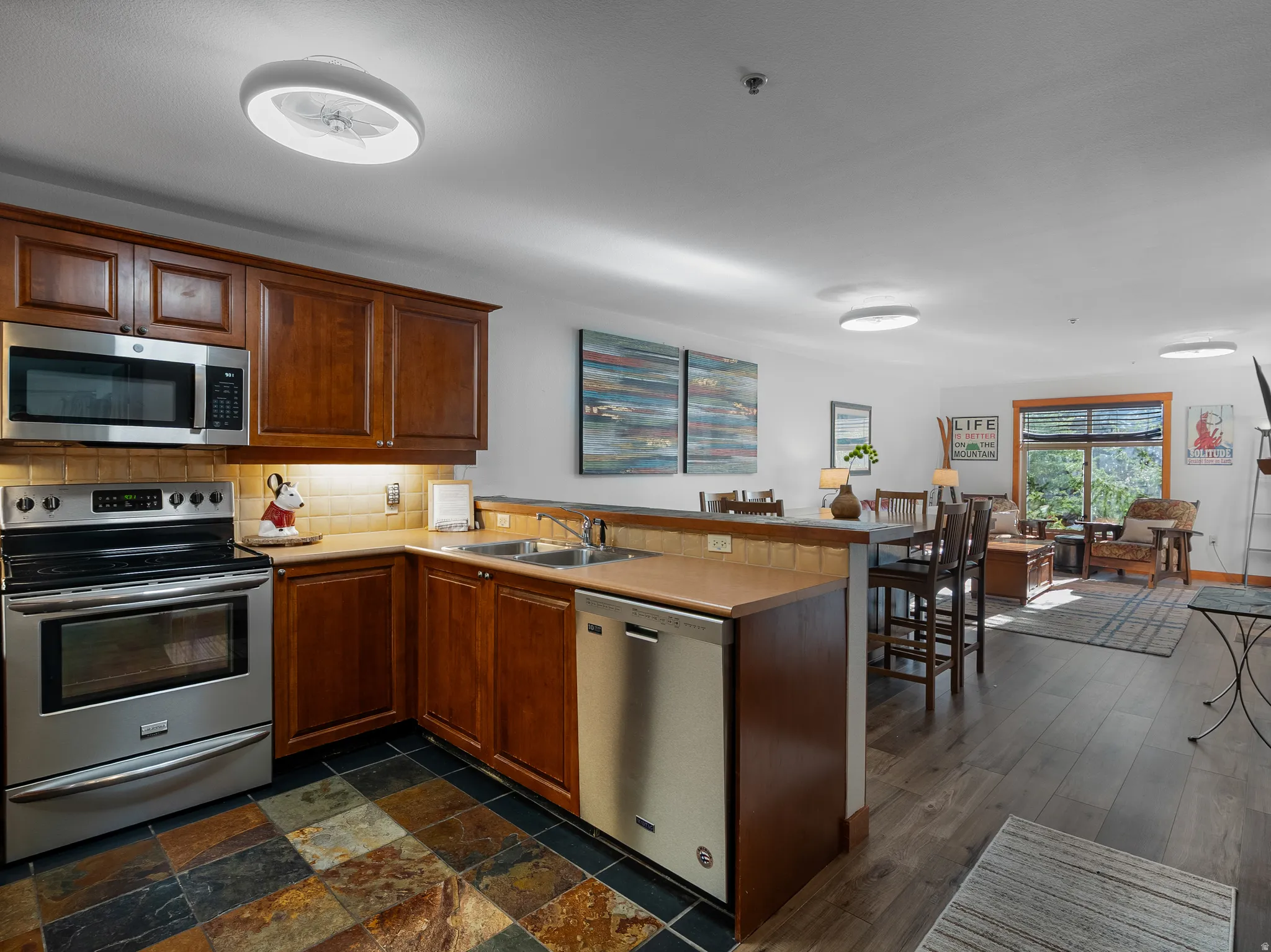 Opposite view from kitchen featuring a peninsula, stainless steel appliances, light countertops, tasteful backsplash, and wood finish cabinets