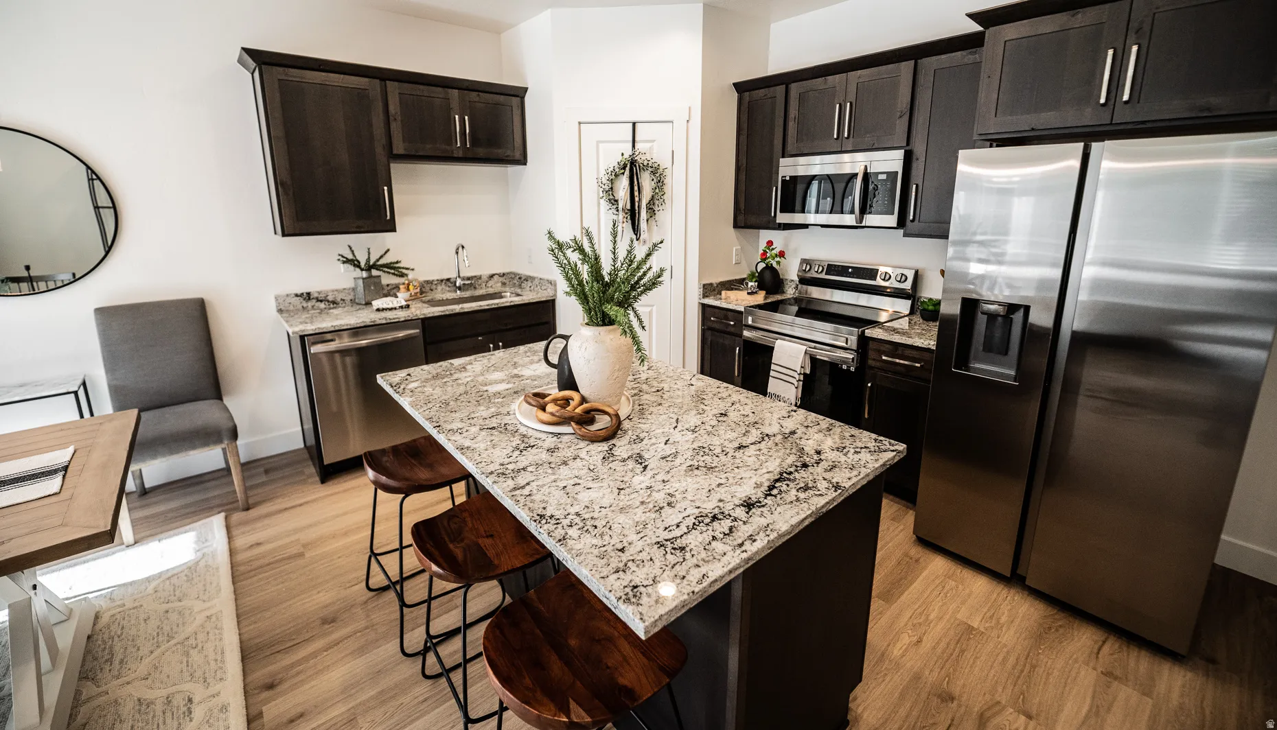 Kitchen with stainless steel appliances, light wood-type flooring, light stone counters, and dark wood finish cabinetry