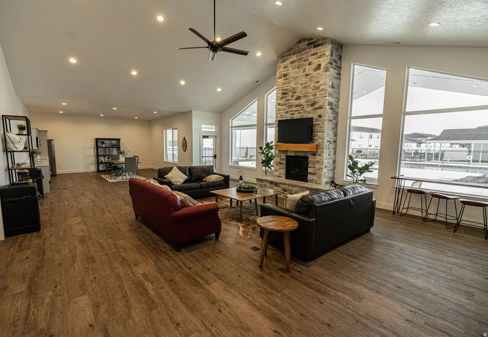 Living area featuring dark wood finished floors, a high ceiling, recessed lighting, a stone fireplace, and a ceiling fan