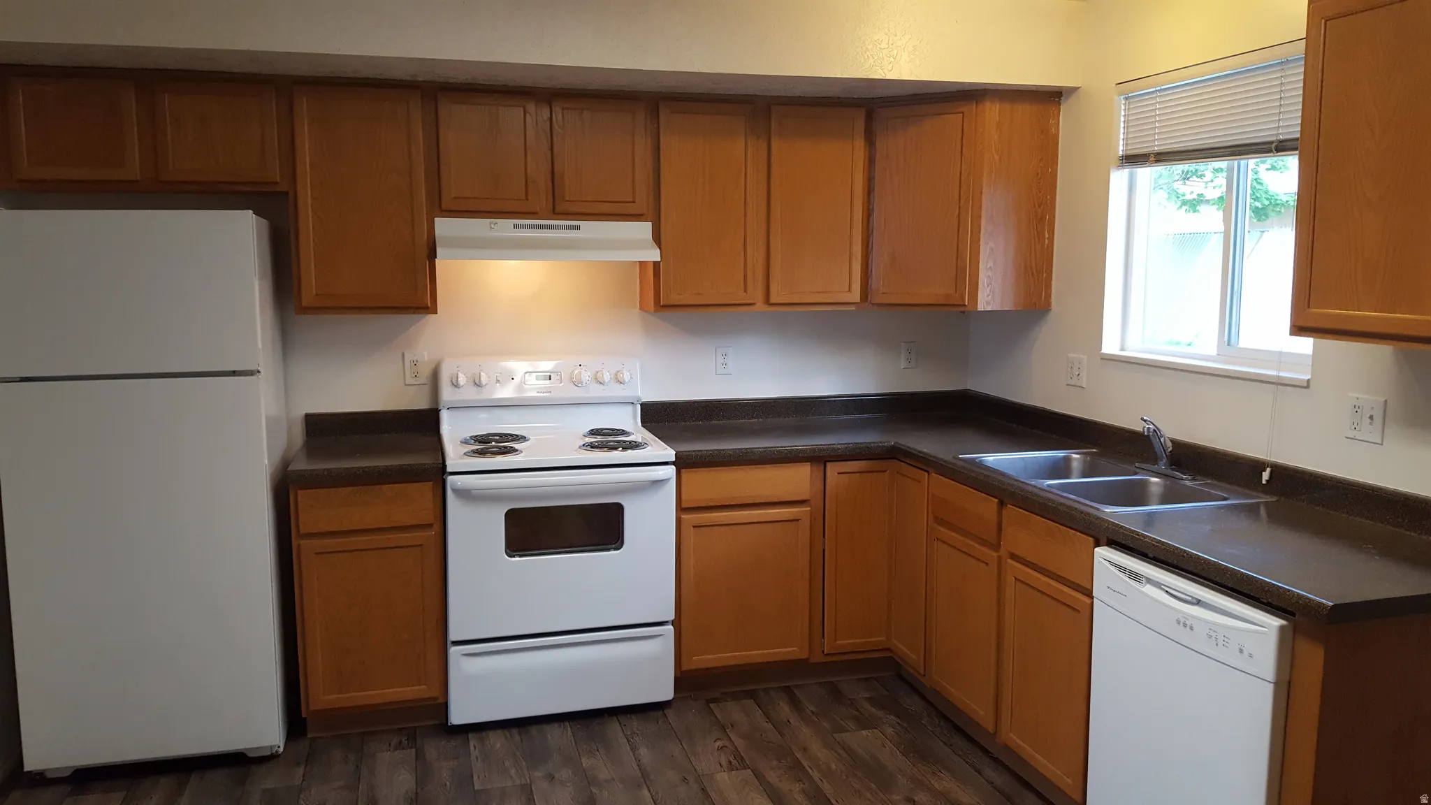 Kitchen with white appliances, dark countertops, wood finish cabinets, and dark wood finished floors