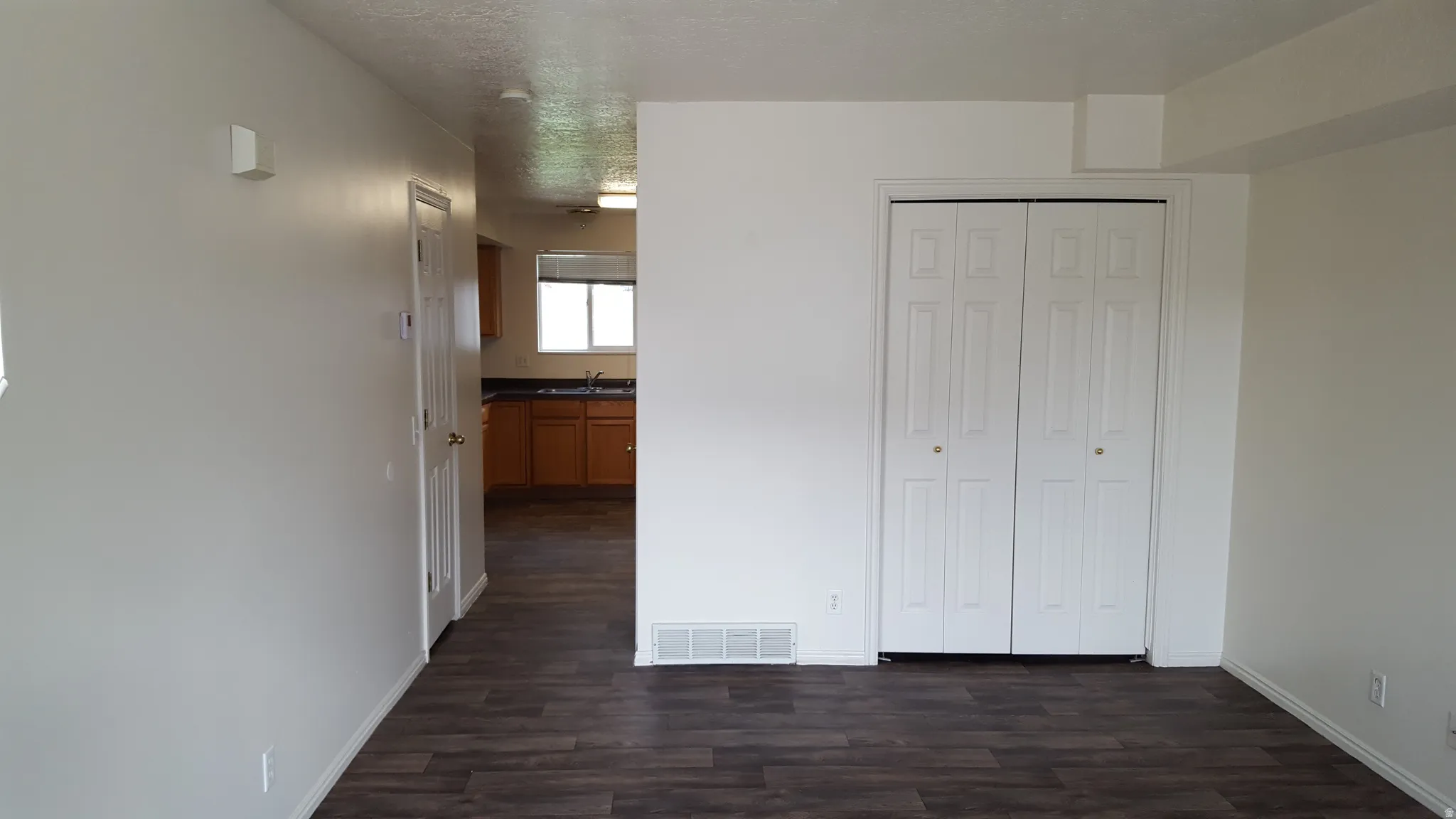 Unfurnished bedroom featuring dark wood-style floors, a closet, a textured ceiling, and ensuite bath