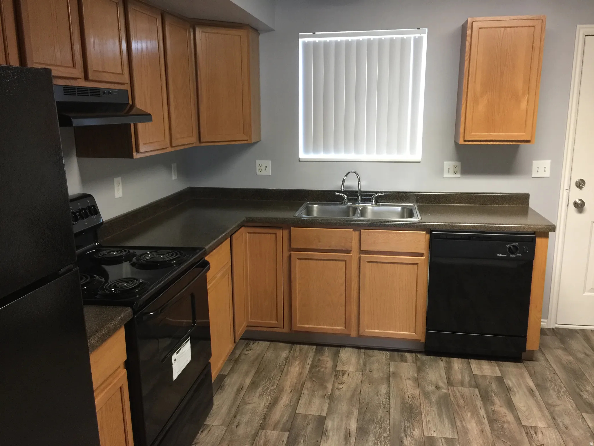 Kitchen with dark countertops, black appliances, wood finish cabinets, and dark wood-style flooring