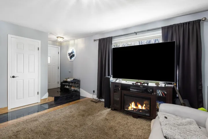 Carpeted living room featuring a glass covered fireplace and baseboards