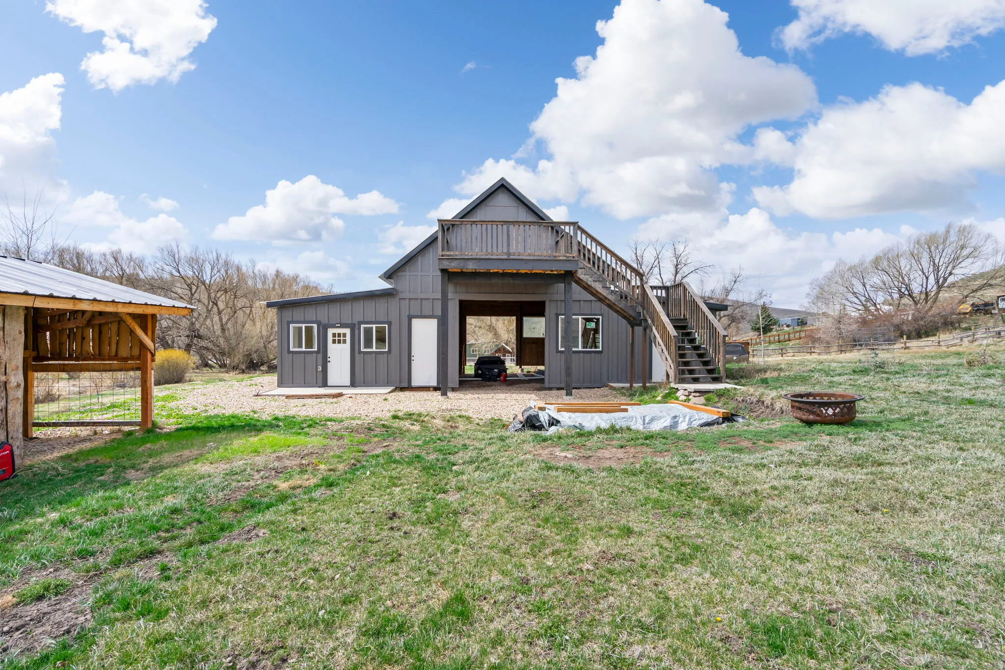 Back of property featuring a patio area, board and batten siding, a deck, an outdoor fire pit, and a lawn