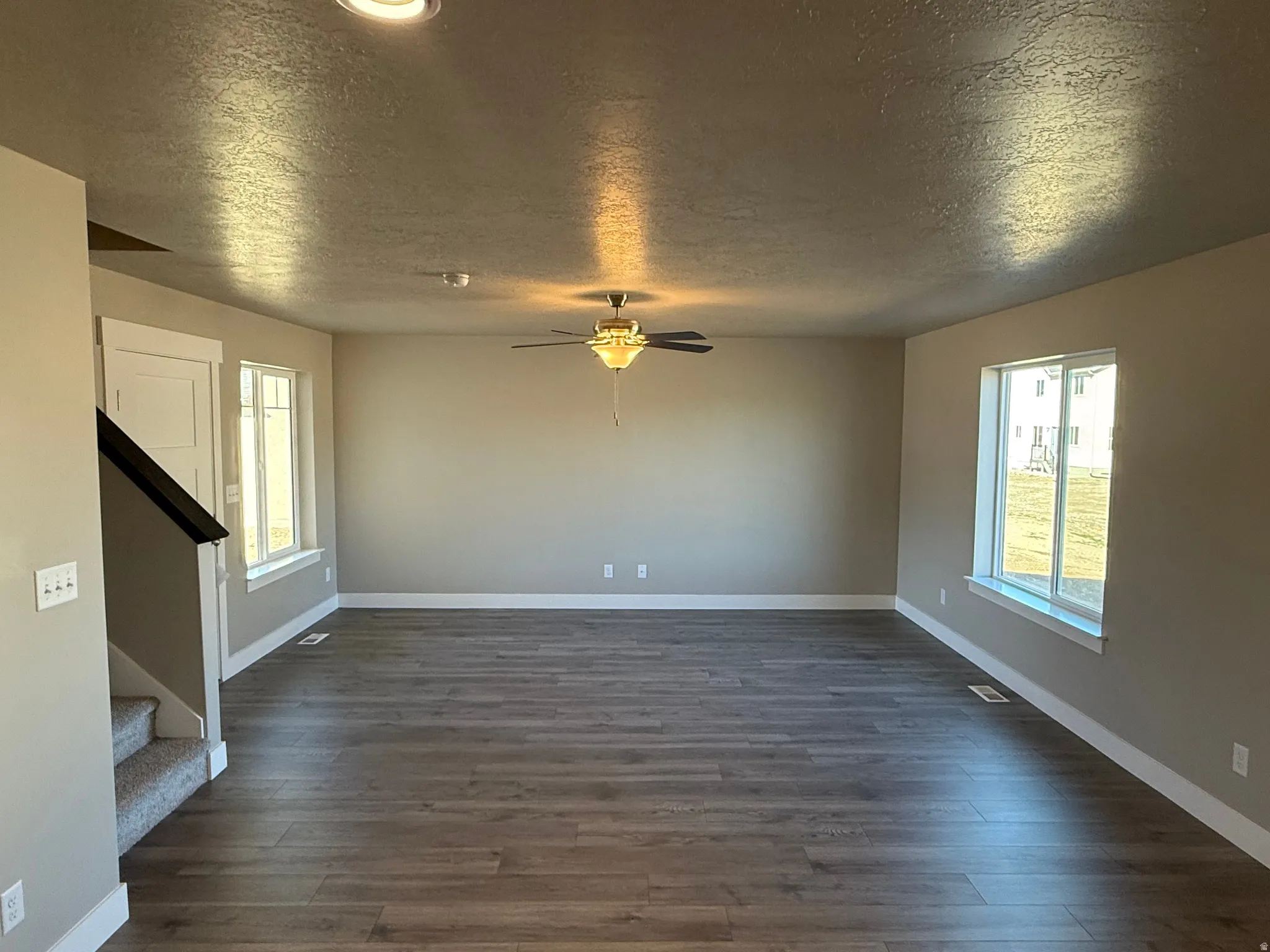 Unfurnished living room featuring a textured ceiling, a ceiling fan, and dark wood finished floors