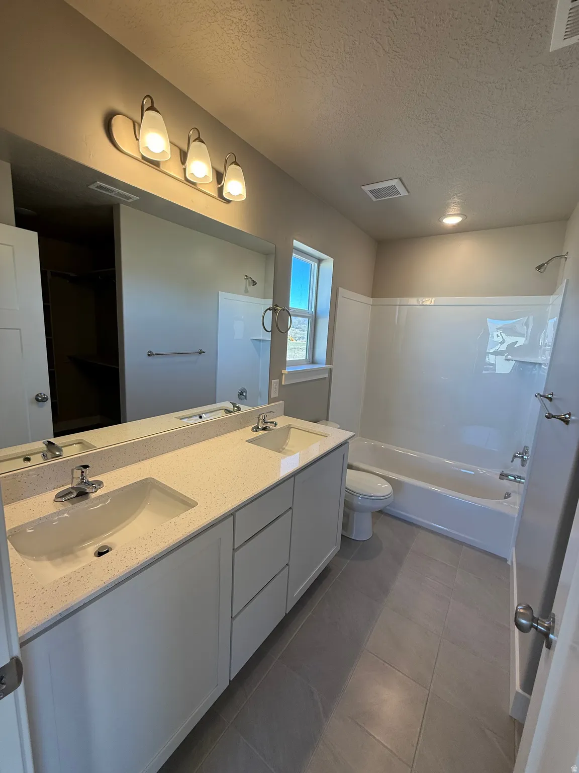 Bathroom featuring double vanity, a textured ceiling, bathtub / shower combination, and dark tile patterned floors