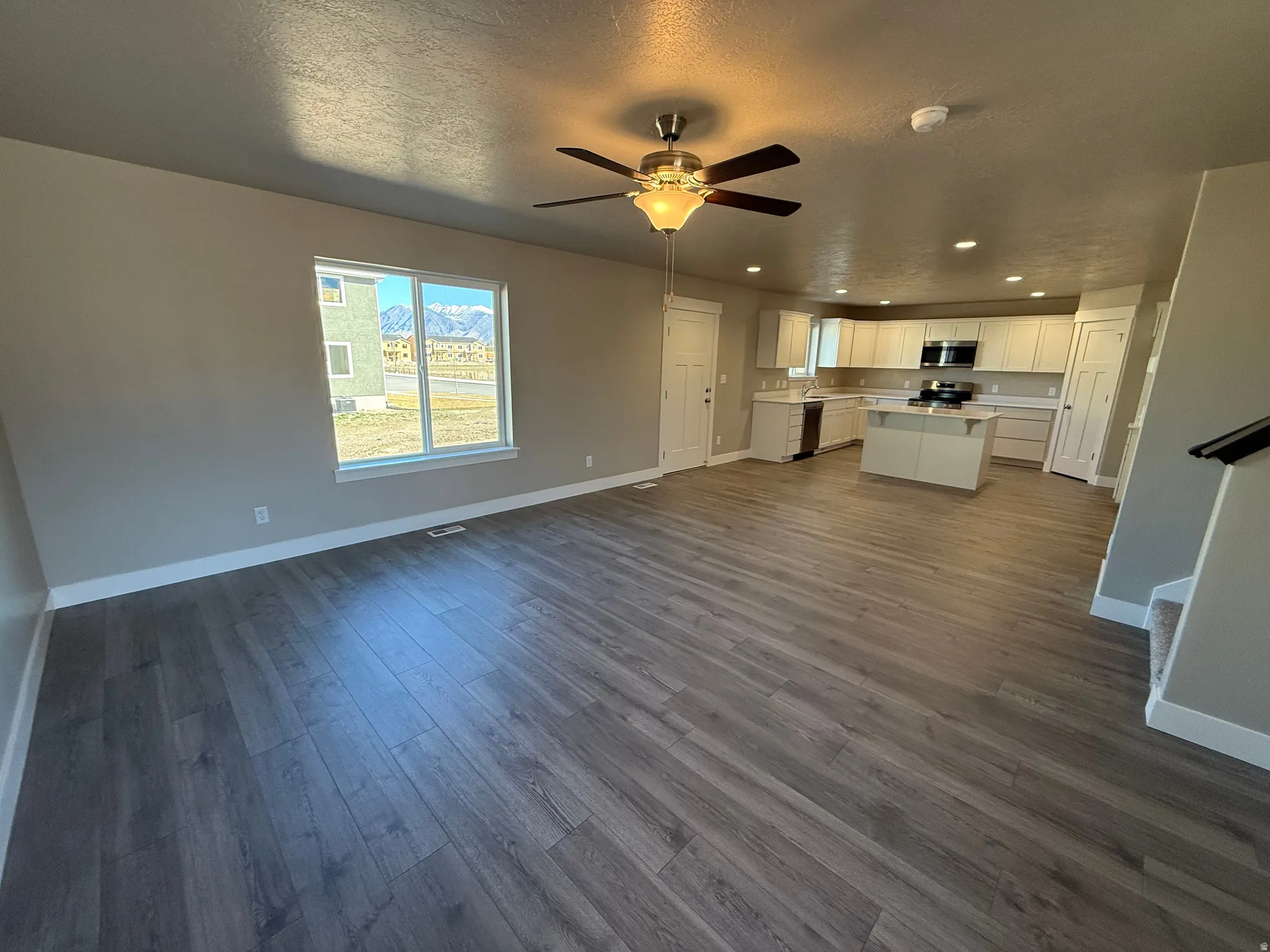 Unfurnished living room featuring dark wood-style floors, recessed lighting, a textured ceiling, and a ceiling fan