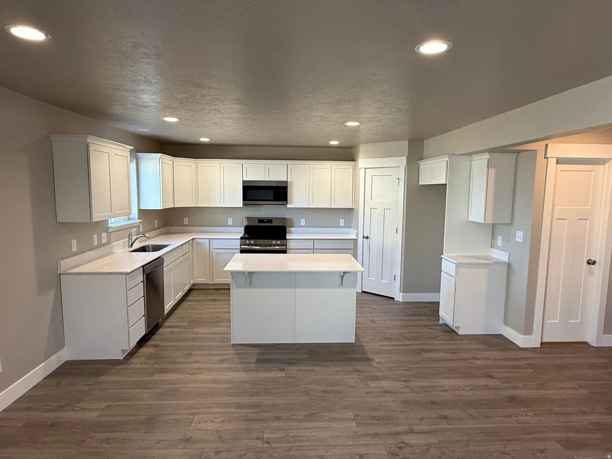 Kitchen featuring stainless steel appliances, white cabinets, dark wood-style floors, a kitchen island, and recessed lighting