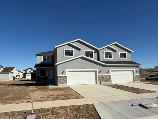 View of front facade featuring driveway, a garage, stucco siding, and stone siding