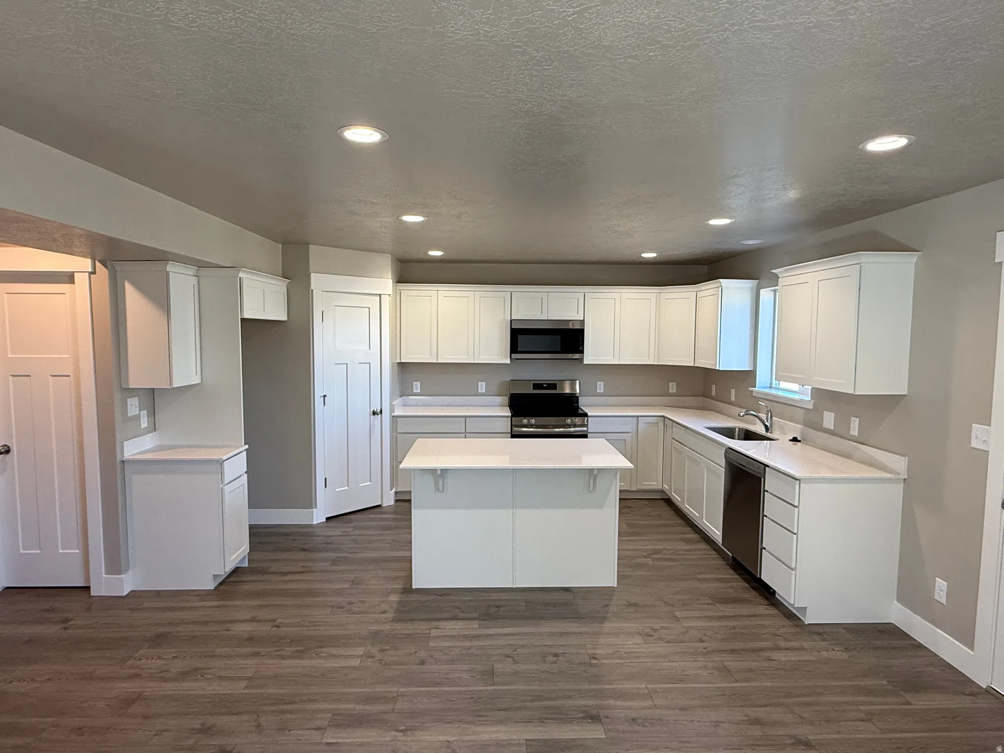 Kitchen featuring stainless steel appliances, recessed lighting, white cabinets, dark wood-style floors, and a center island