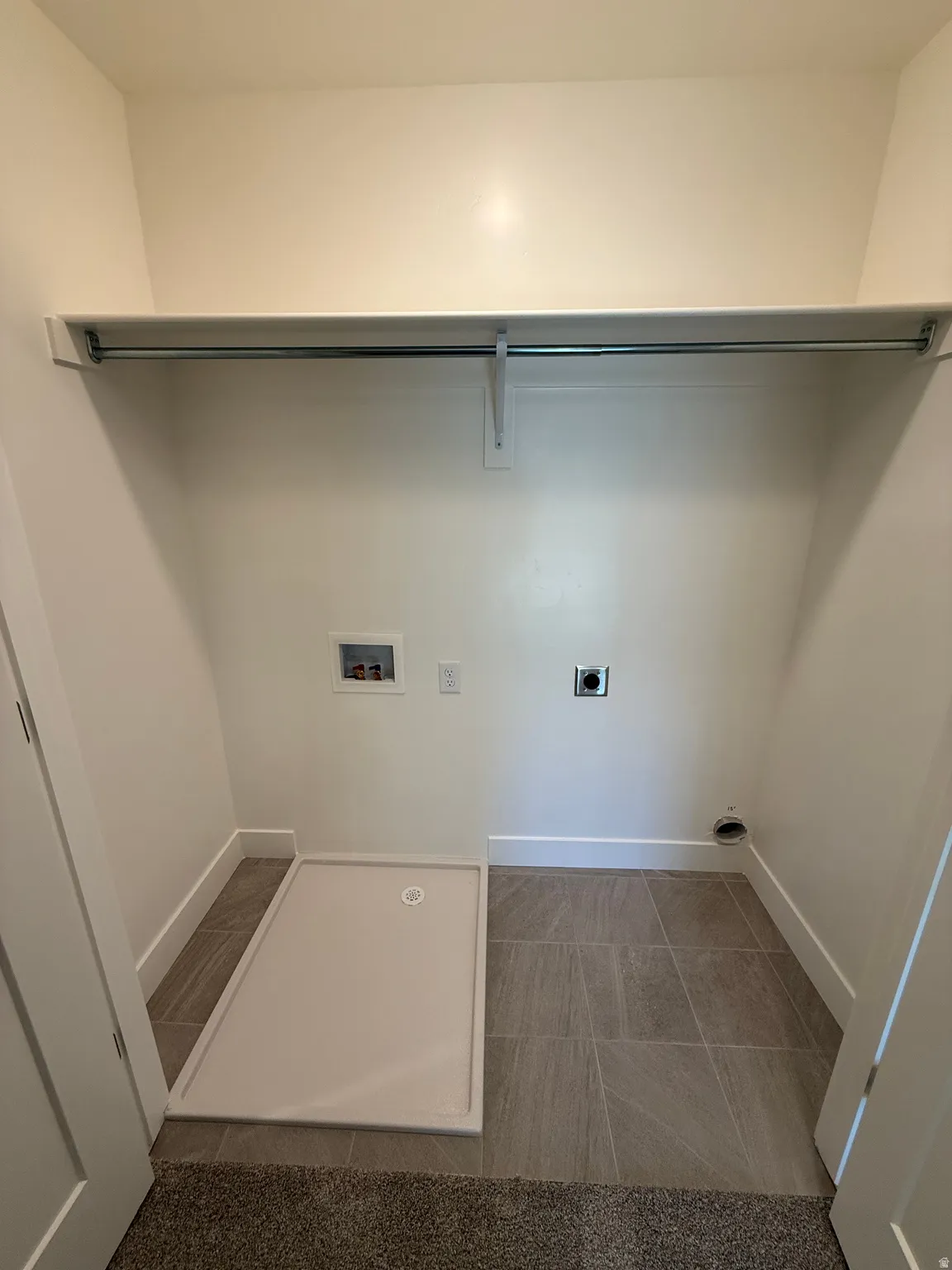 Laundry area with hookup for an electric dryer, hookup for a washing machine, and dark tile patterned flooring