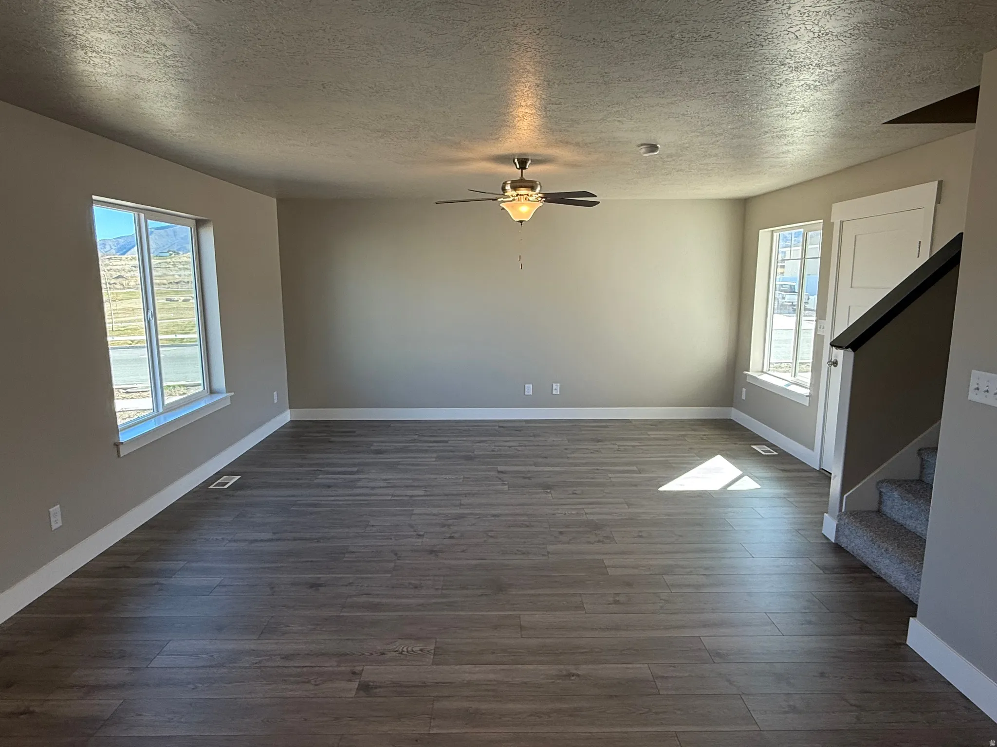 Unfurnished living room with a textured ceiling, dark wood-style flooring, and a ceiling fan