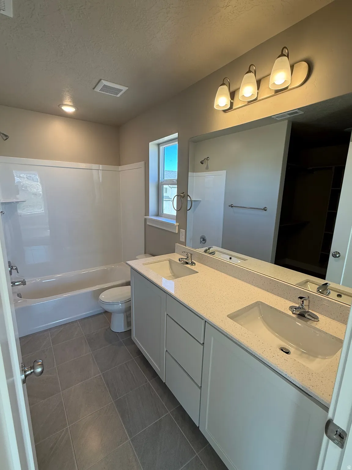 Full bathroom with double vanity, a textured ceiling, shower / tub combination, and dark tile patterned floors