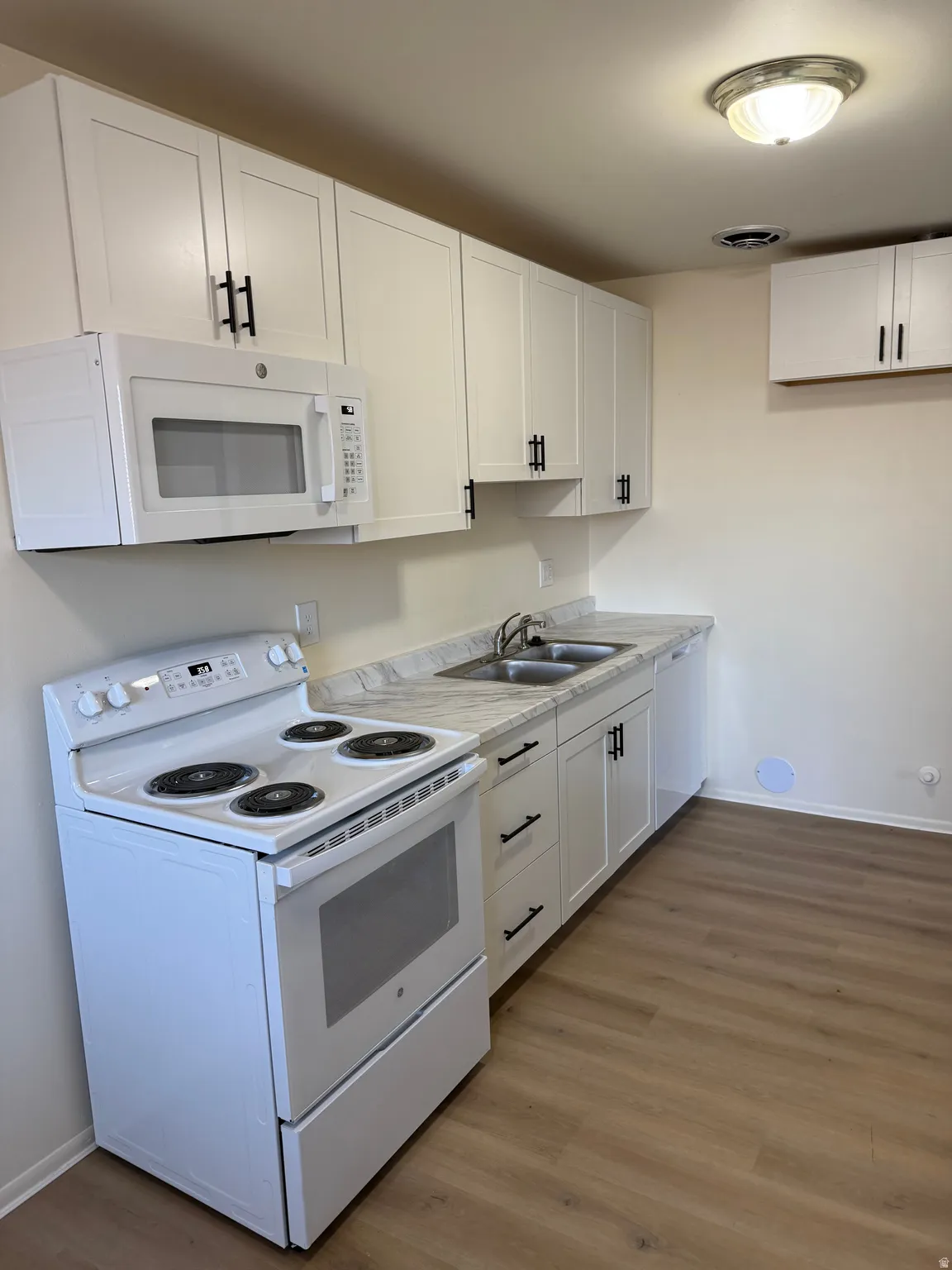 Kitchen featuring white appliances, white cabinetry, light countertops, and dark wood-type flooring