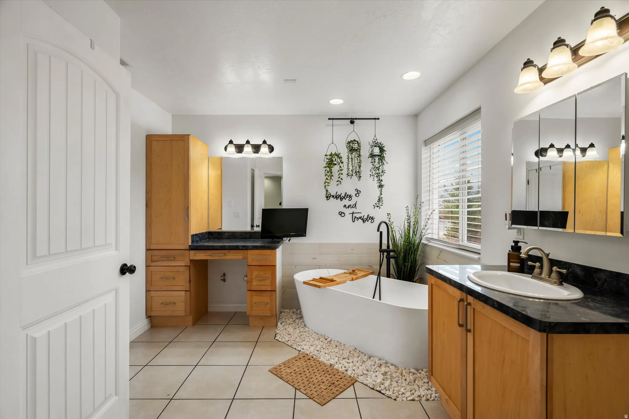Bathroom featuring two vanities, a freestanding tub, light tile patterned floors, and recessed lighting