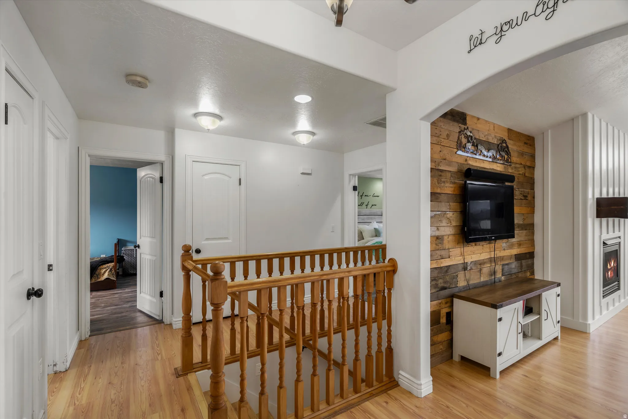 Hall with an upstairs landing, light wood-style flooring, and arched walkways
