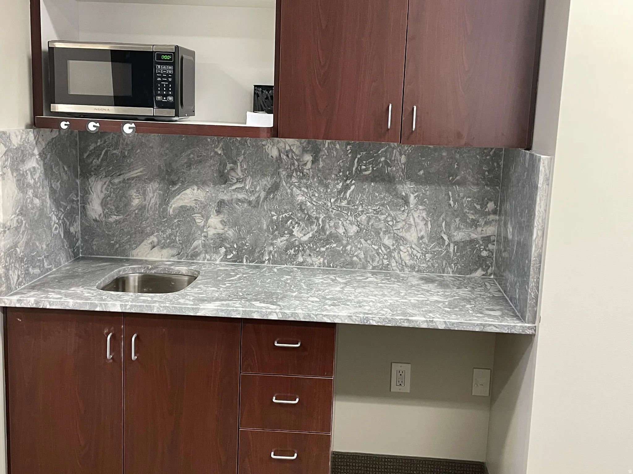 Kitchen featuring stainless steel microwave, tasteful backsplash, modern cabinets, light stone countertops, and dark wood finish cabinetry