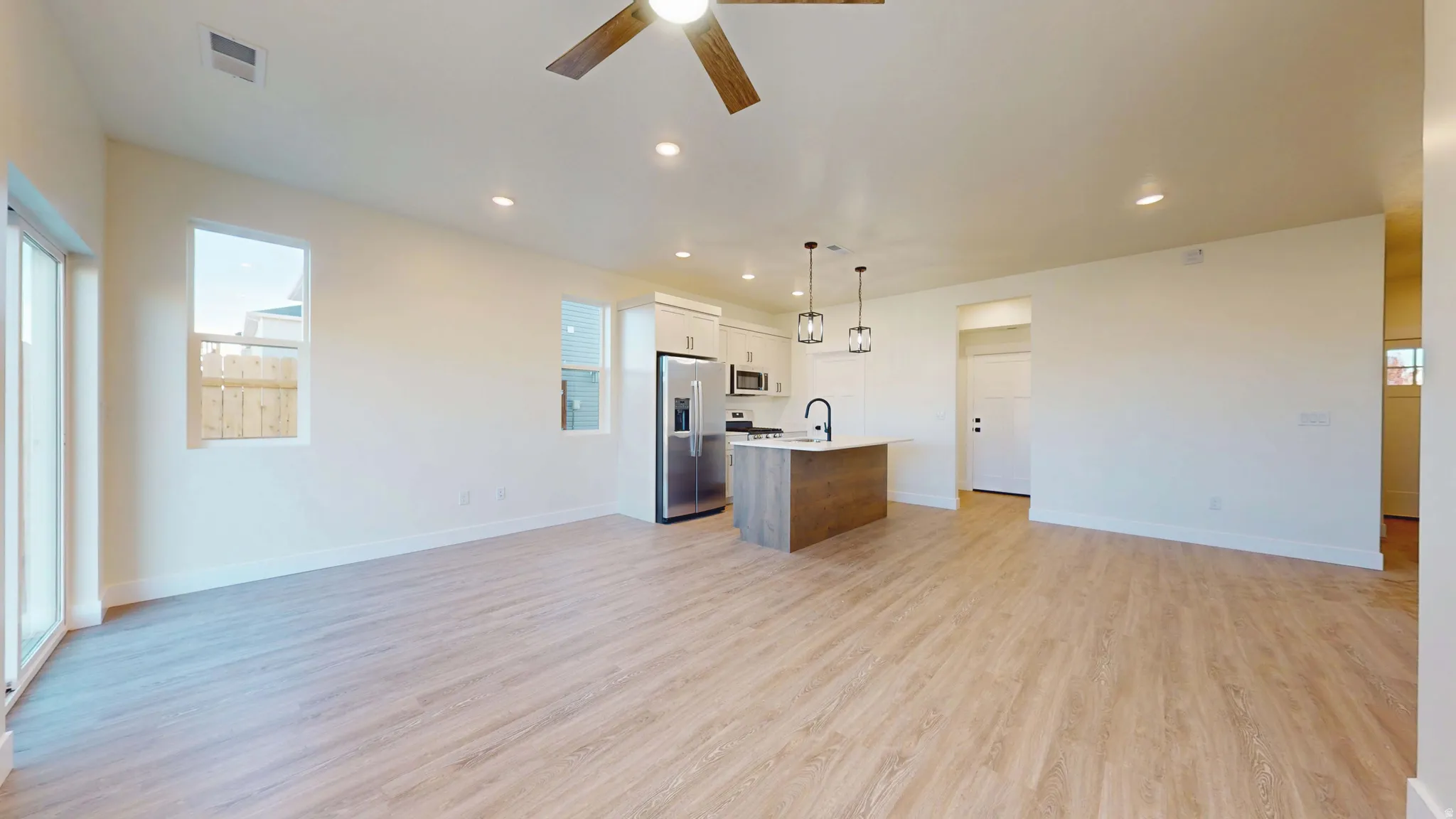 Kitchen featuring open floor plan, stainless steel appliances, a center island with sink, decorative light fixtures, and a ceiling fan
