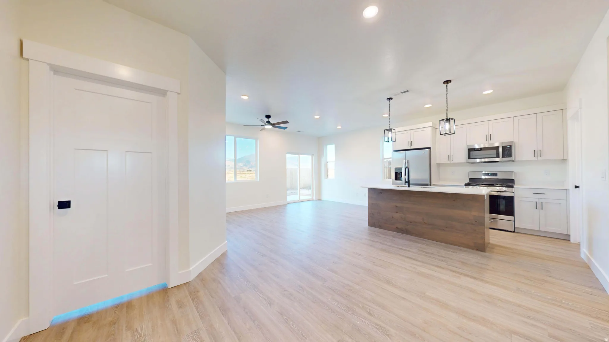 Two tone kitchen featuring open floor plan, stainless steel appliances, light countertops, light wood-type flooring, and an island with sink