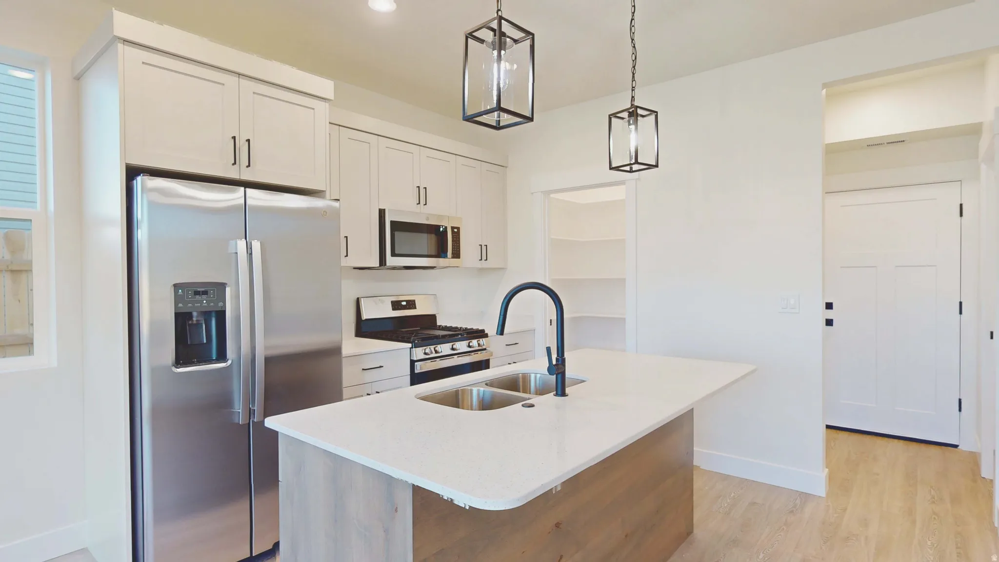 Kitchen with stainless steel appliances, an island with sink, light wood-style flooring, pendant lighting, and white cabinets