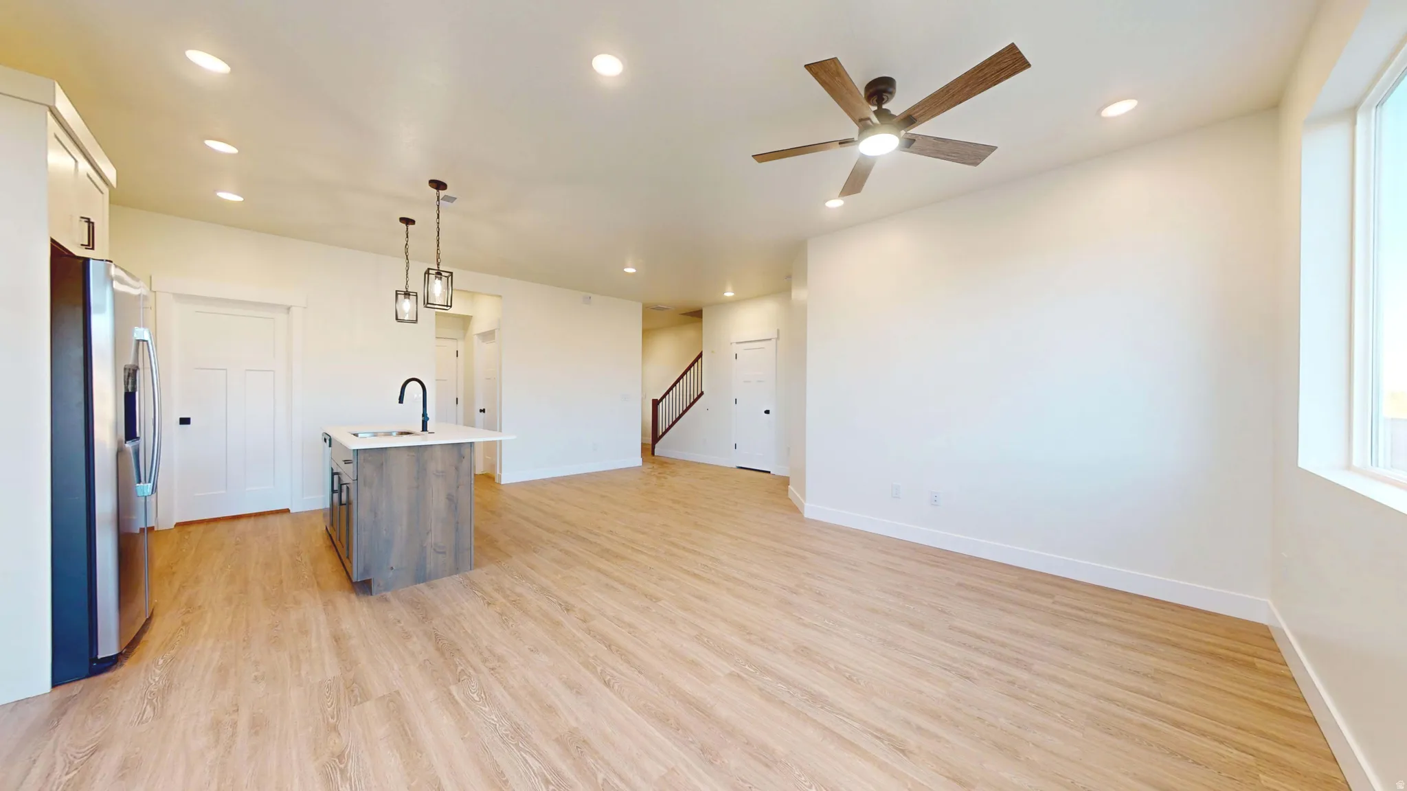 Kitchen with an island with sink, open floor plan, stainless steel fridge, light wood-style flooring, and pendant lighting