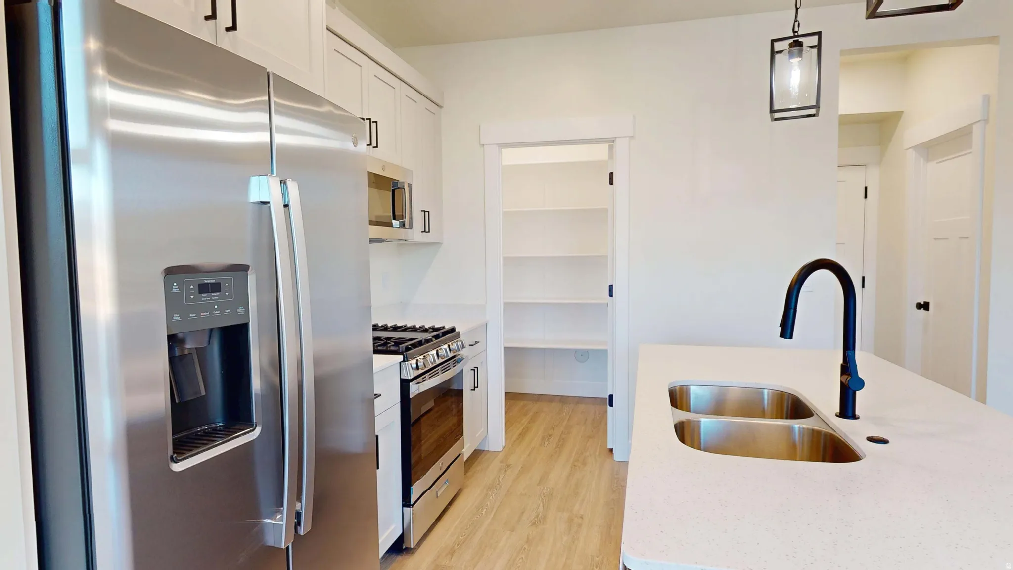 Kitchen featuring stainless steel appliances, pendant lighting, light wood-style flooring, white cabinets, and light stone counters