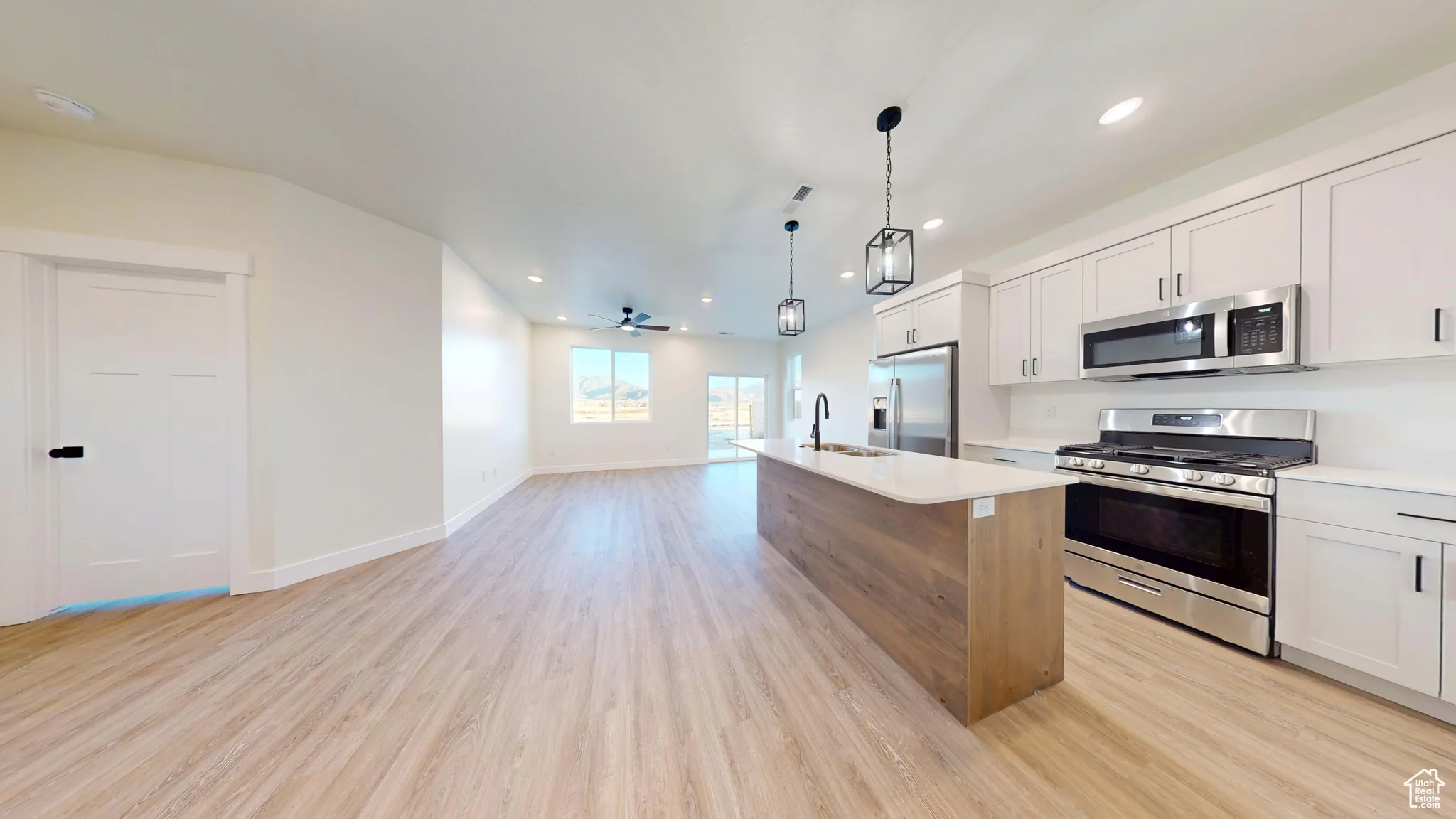 Dual tone kitchen featuring stainless steel appliances, open floor plan, light wood finished floors, ceiling fan, and a kitchen island with sink
