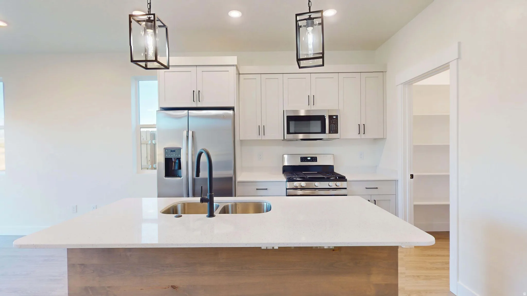 Kitchen with stainless steel appliances, light stone countertops, a center island with sink, light wood-type flooring, and decorative light fixtures