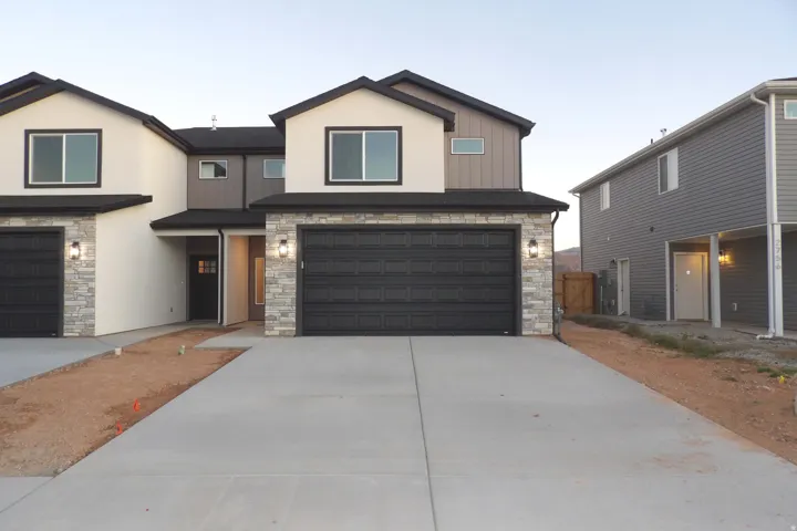 View of front facade featuring stone siding, driveway, a garage, and stucco siding