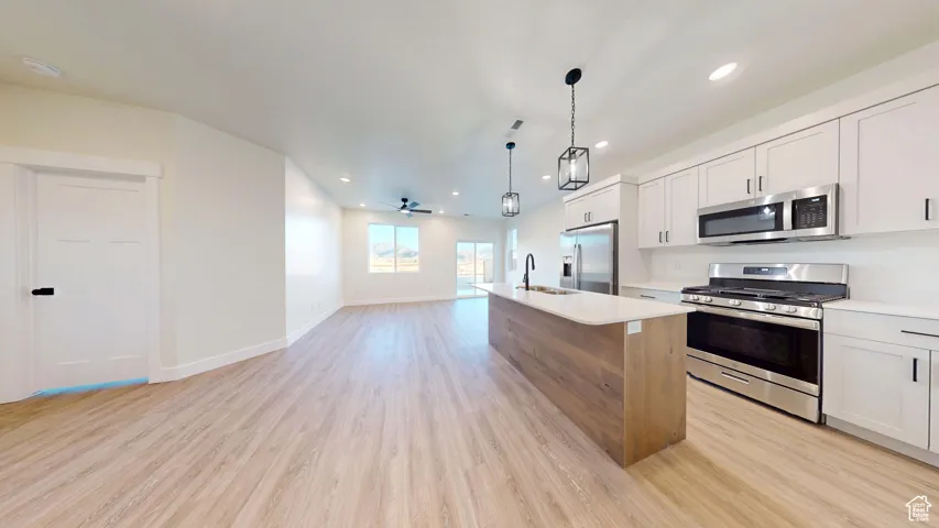 Dual tone kitchen featuring stainless steel appliances, open floor plan, light wood finished floors, ceiling fan, and a kitchen island with sink