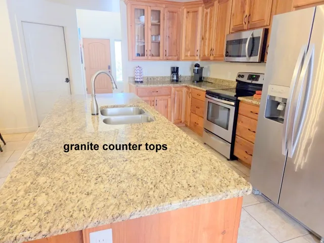 Kitchen with light tile patterned flooring, glass insert cabinets, stainless steel appliances, and light granite countertops