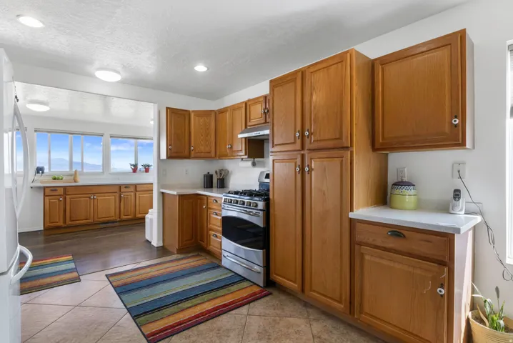 Kitchen with stainless steel gas range, light countertops, wood finish cabinetry, freestanding refrigerator, and recessed lighting