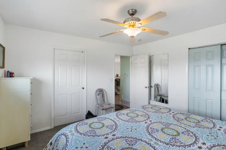 Bedroom with two closets, dark carpet, and a ceiling fan
