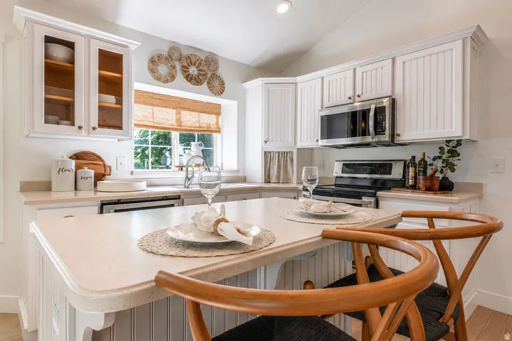 Kitchen featuring white cabinetry with beadboard paneling, a breakfast bar, stainless steel appliances, a double basin sink, and a window with natural light