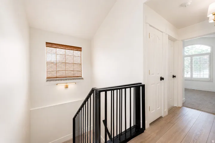 Staircase featuring a modern black iron railing, wood-finish flooring, a window with a woven shade, and a wall-mounted light fixture