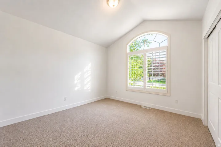 Arched window with custom plantation shutters, neutral wall finishes, textured carpet flooring, and a standard white ceiling light fixture