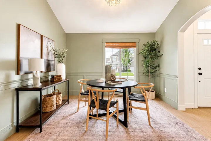 Dining area featuring wainscoting, light green walls, wood-finish flooring, a window with a woven shade, and an arched entry