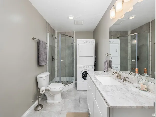 Bathroom with vanity, a stall shower, stacked washer / dryer, and light tile patterned floors