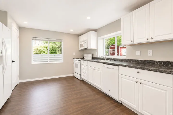 Kitchen featuring white cabinetry, dark speckled countertops, and wood-finish flooring