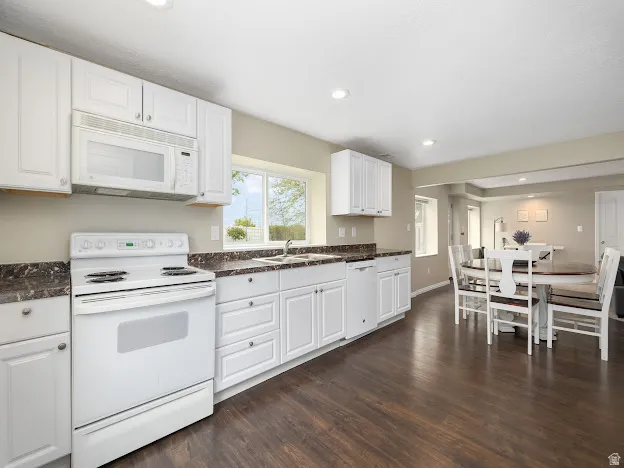 Kitchen with white appliances, recessed lighting, white cabinets, dark wood-style floors, and dark stone countertops