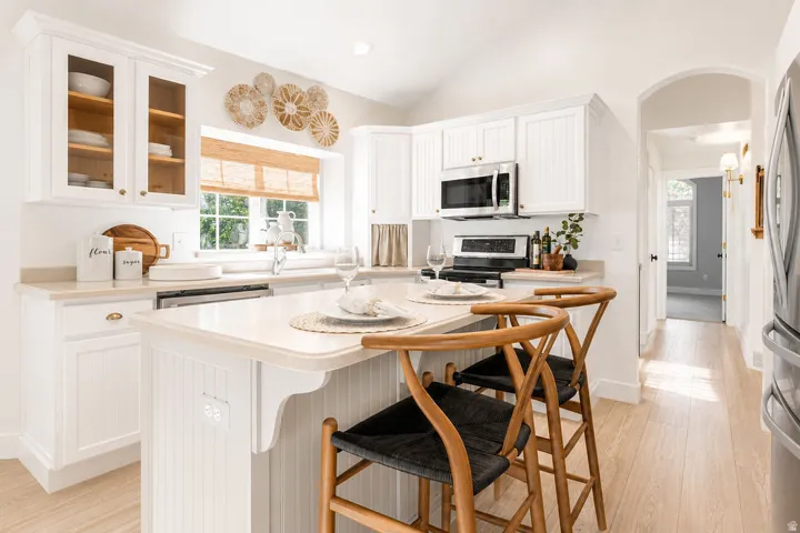 Bright kitchen featuring white cabinetry, a central island with seating, stainless steel appliances, a window above the sink, and wood-finish flooring