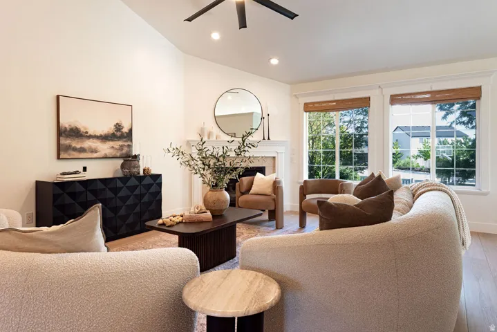 Spacious living area featuring a vaulted ceiling with a ceiling fan, light wood-finish flooring, and a decorative fireplace with a mantel