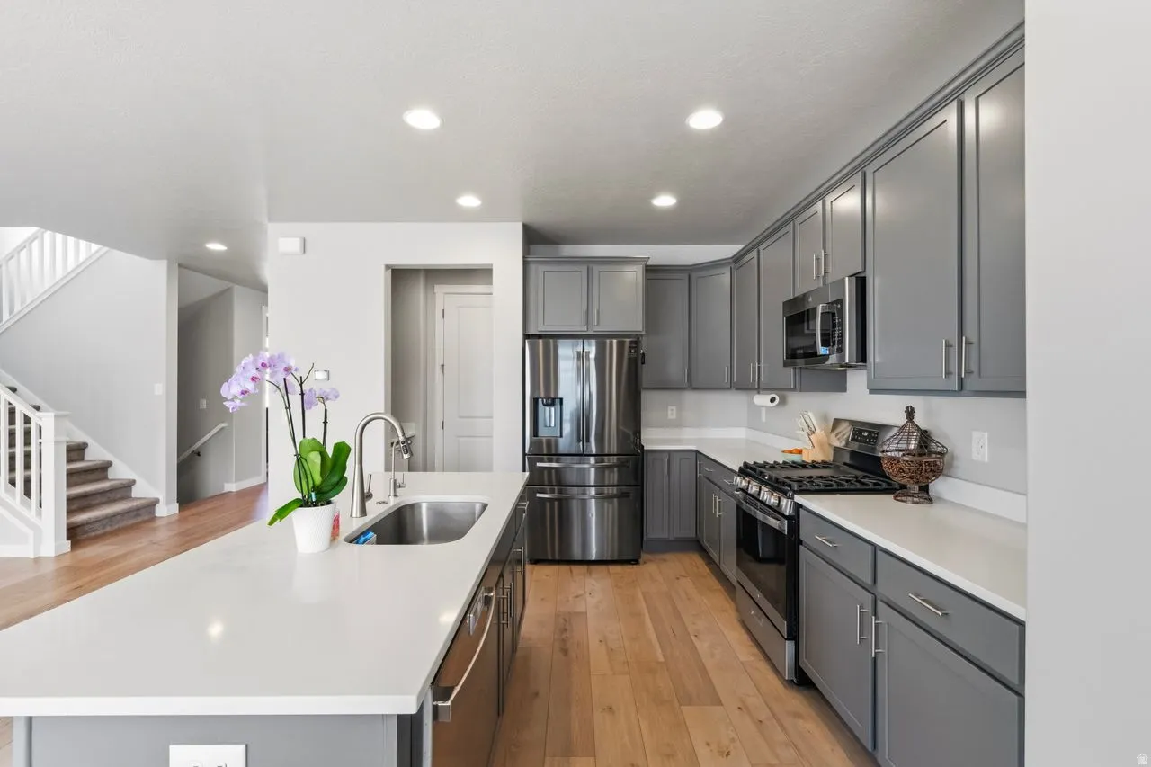Kitchen with gray cabinets, stainless steel appliances, a kitchen island with sink, light wood finished floors, and recessed lighting